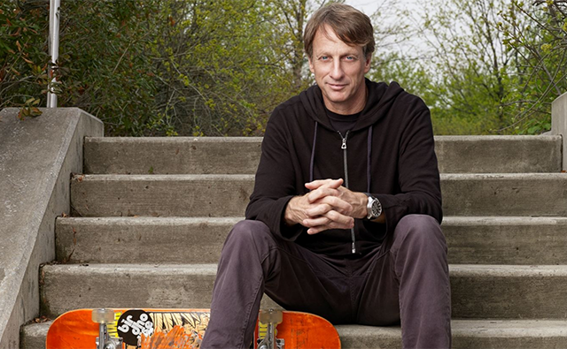 Tony Hawk posed with a skateboard on a staircase. 