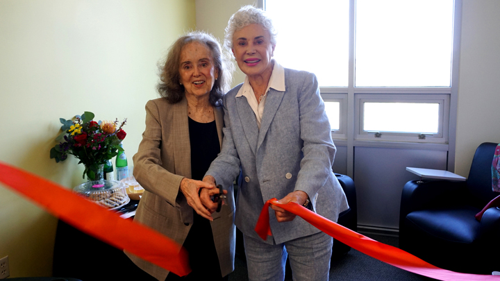 two women hold scissors and cut red ribbon