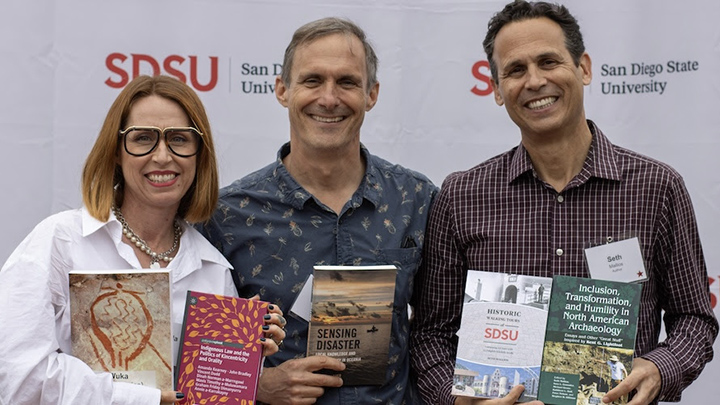 one female and two male faculty smile and hold books