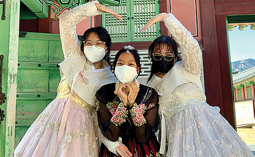 three students in southeast asian costumes pose near structure