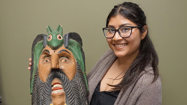 woman with glasses holds Mesoamerican mask of man with beard