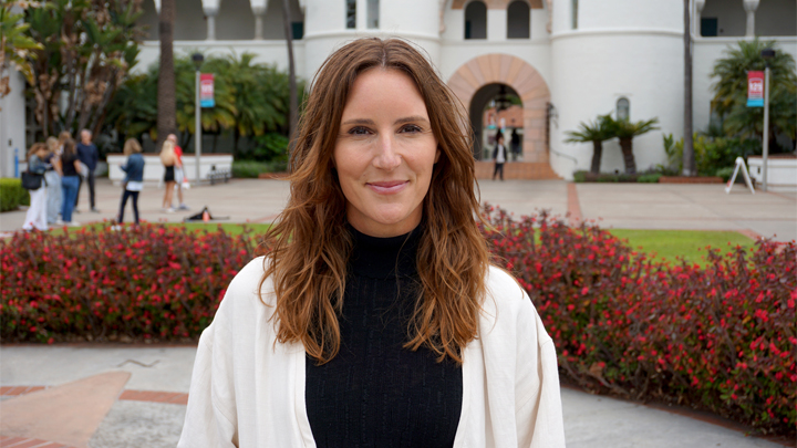 smiling woman with long brown hair stands outside of Hepner Hall, SDSU