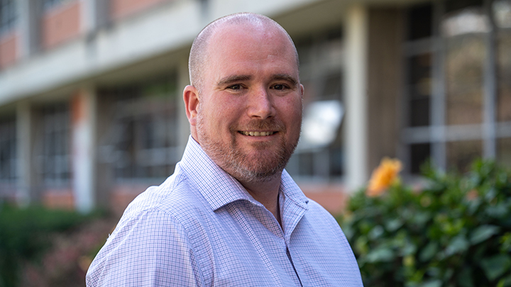 man smiles standing in front of school