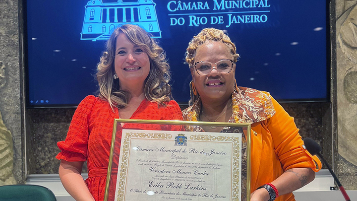 two women hold plague, screen behind them says Camara Municipal Rio de Janero