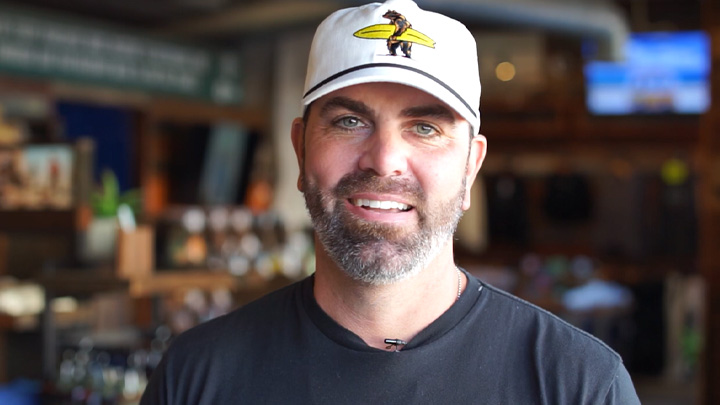 man wearing baseball hat with bear holding surfboard on it