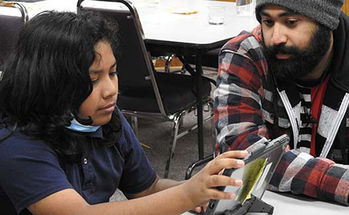 student look at tablet with help of volunteer