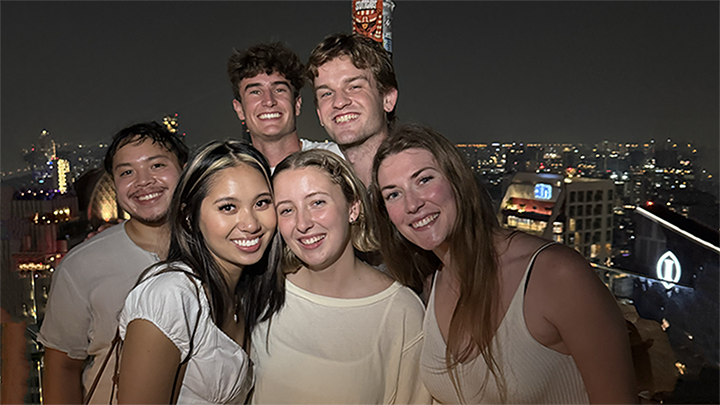 group of students pose at night in front of skyline