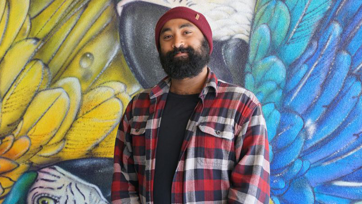 man with beard stands in front of colorful mural