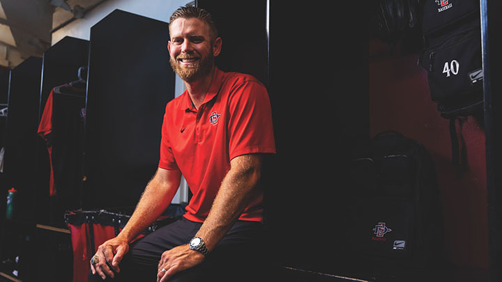 Man sits in locker room wearing a red SDSU polo shirt