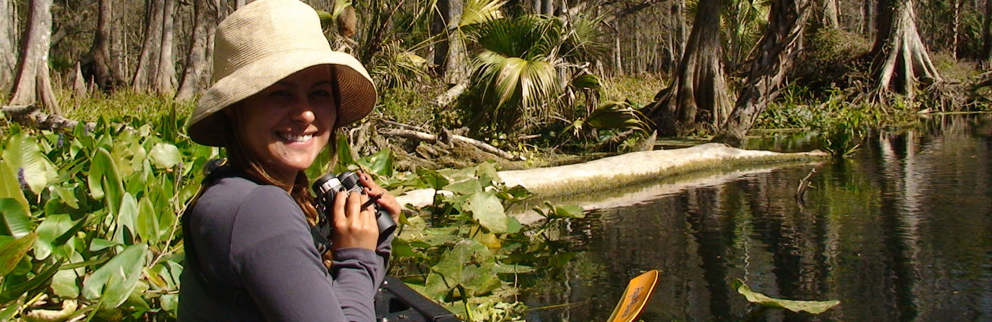 female student in canoe and holding binoculars